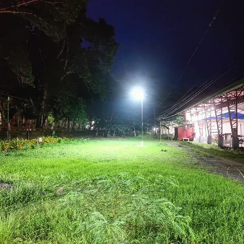 Il lampione solare Sungreat Energy serie QH illumina di notte un'ampia area erbosa e un capannone industriale, dimostrando una potente copertura luminosa ad ampio angolo.
